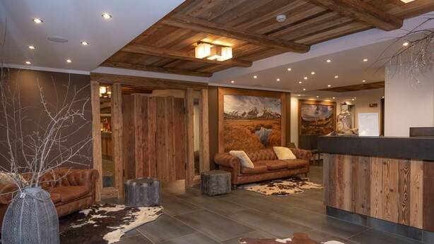 A modern lobby with a wooden ceiling, leather sofas, a reception desk, and a large wall painting. - Hotel Gran Roc (Sestriere)