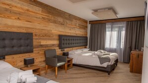 A modern hotel room with a wooden wall panel, a large bed, a smaller bed, a desk, and a chair. - Hotel Gran Roc (Sestriere)