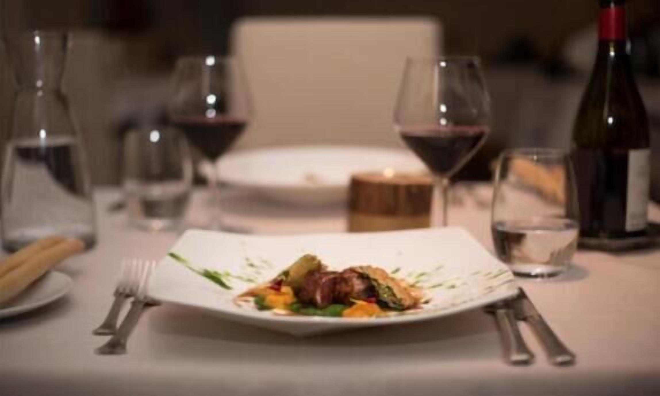 A dining table with a plate of food, wine glasses, and bottles.