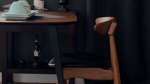 Un suelo de madera, una cortina oscura, una mesa con un sombrero, una planta y una silla.