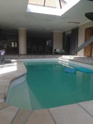 A swimming pool with a clear view of the surrounding area, including a covered patio and a dining area. - Shirleys Place (Cape Town)