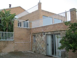 A two-story brick house with a balcony, a sliding glass door, and a small patio area. - Shirleys Place (Cape Town)