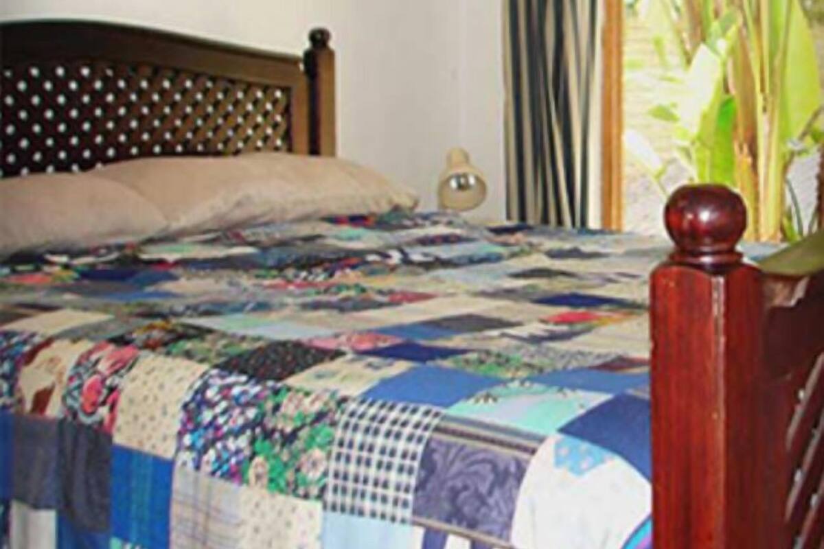 A bedroom with a wooden bed frame, a colorful quilt, a bedside lamp, and a curtain.