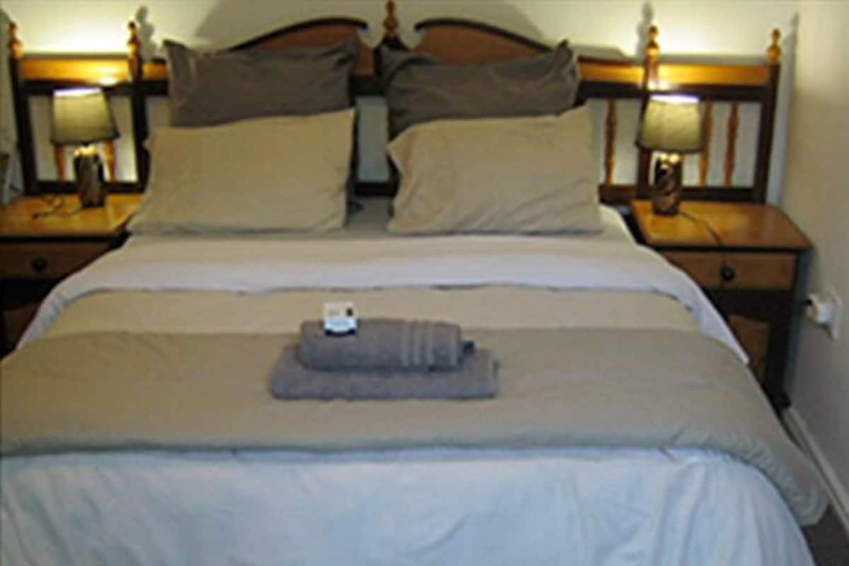 A neatly made bed with a gray blanket and two pillows, a small towel, and two bedside lamps on wooden nightstands.