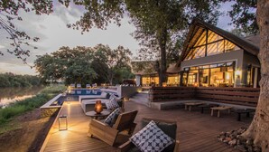 Un terrazzo in legno con posti a sedere esterni, una piscina e un edificio con ampie finestre.
