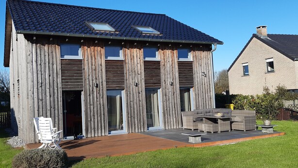 A modern house with a wooden facade, large windows, and a patio with outdoor furniture. - WOODEN HOUSE, chalet style (Lontzen)