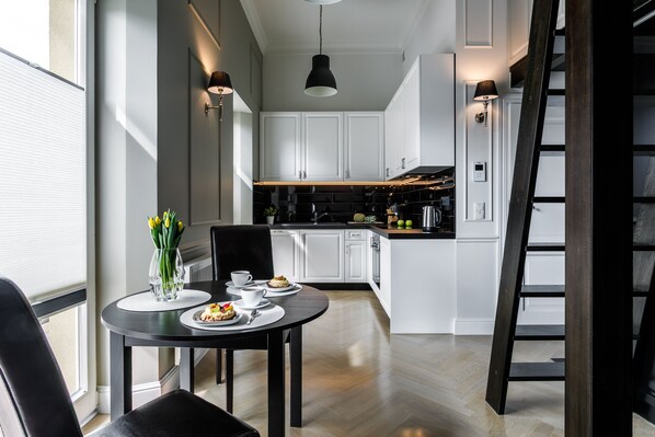 Een moderne keuken met witte kasten, een eettafel met stoelen en een trap.
