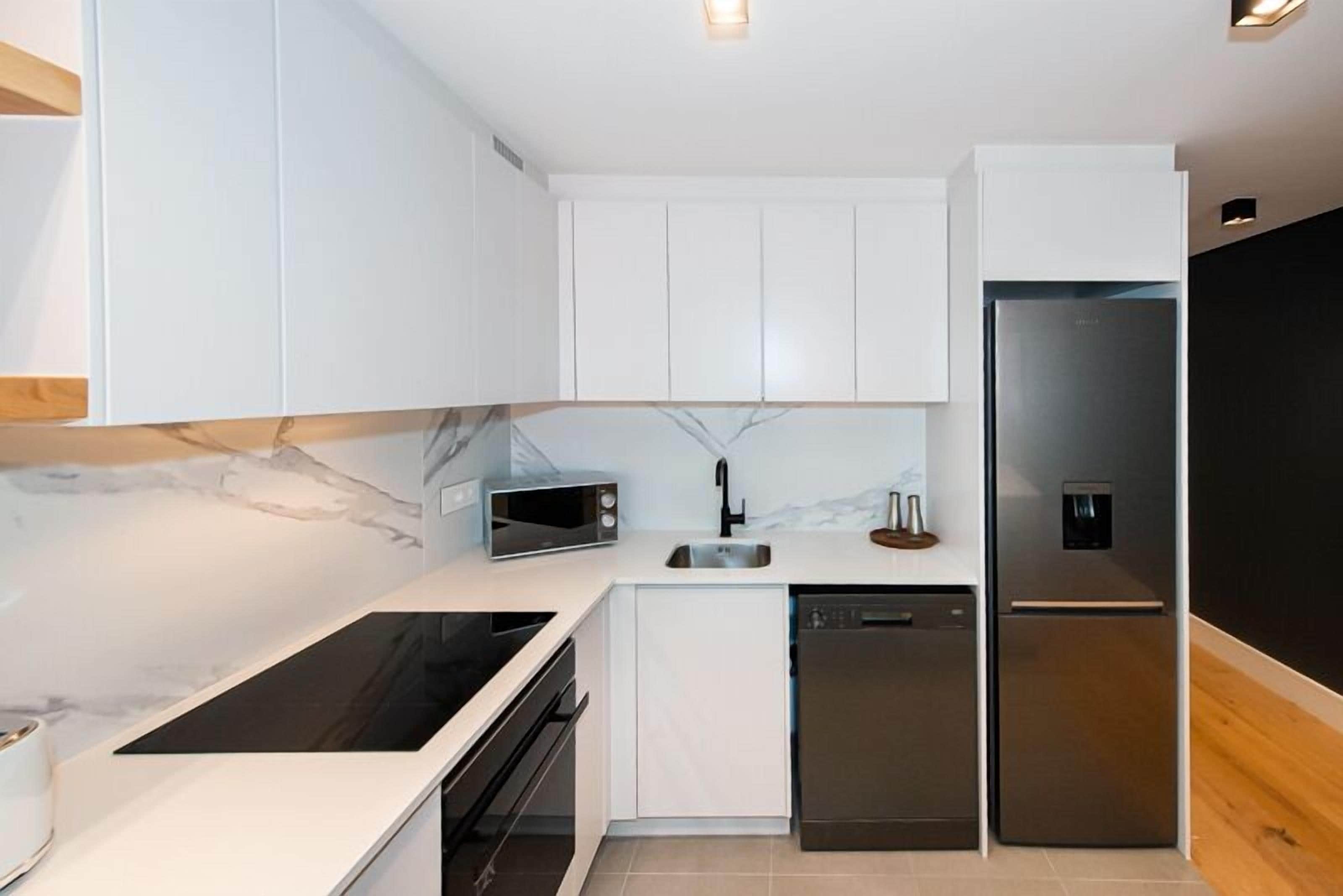 A modern kitchen with white cabinetry, a built-in microwave, a stainless steel refrigerator, and a dishwasher.