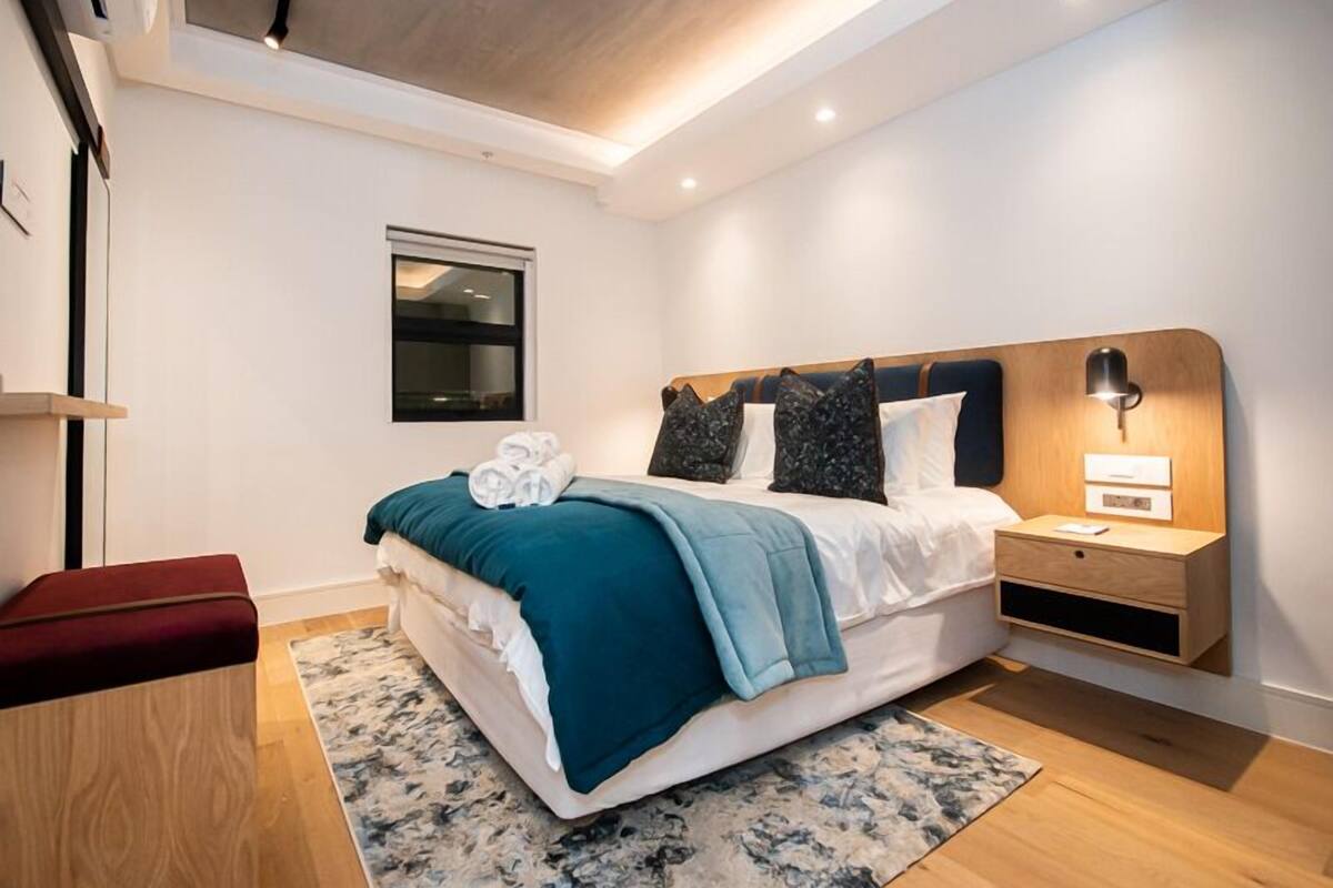 A modern hotel room with a bed, a nightstand, a desk, and a window.