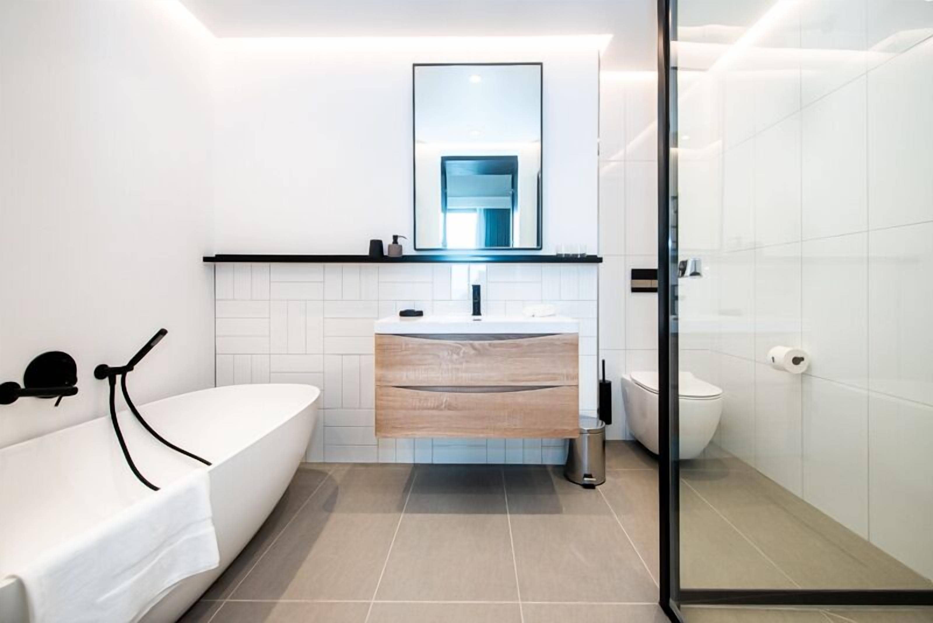 A modern bathroom with a freestanding bathtub, a wooden vanity, a mirror above the sink, and a toilet.