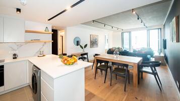 A modern kitchen with white cabinetry, a wooden dining table, and a fruit bowl.