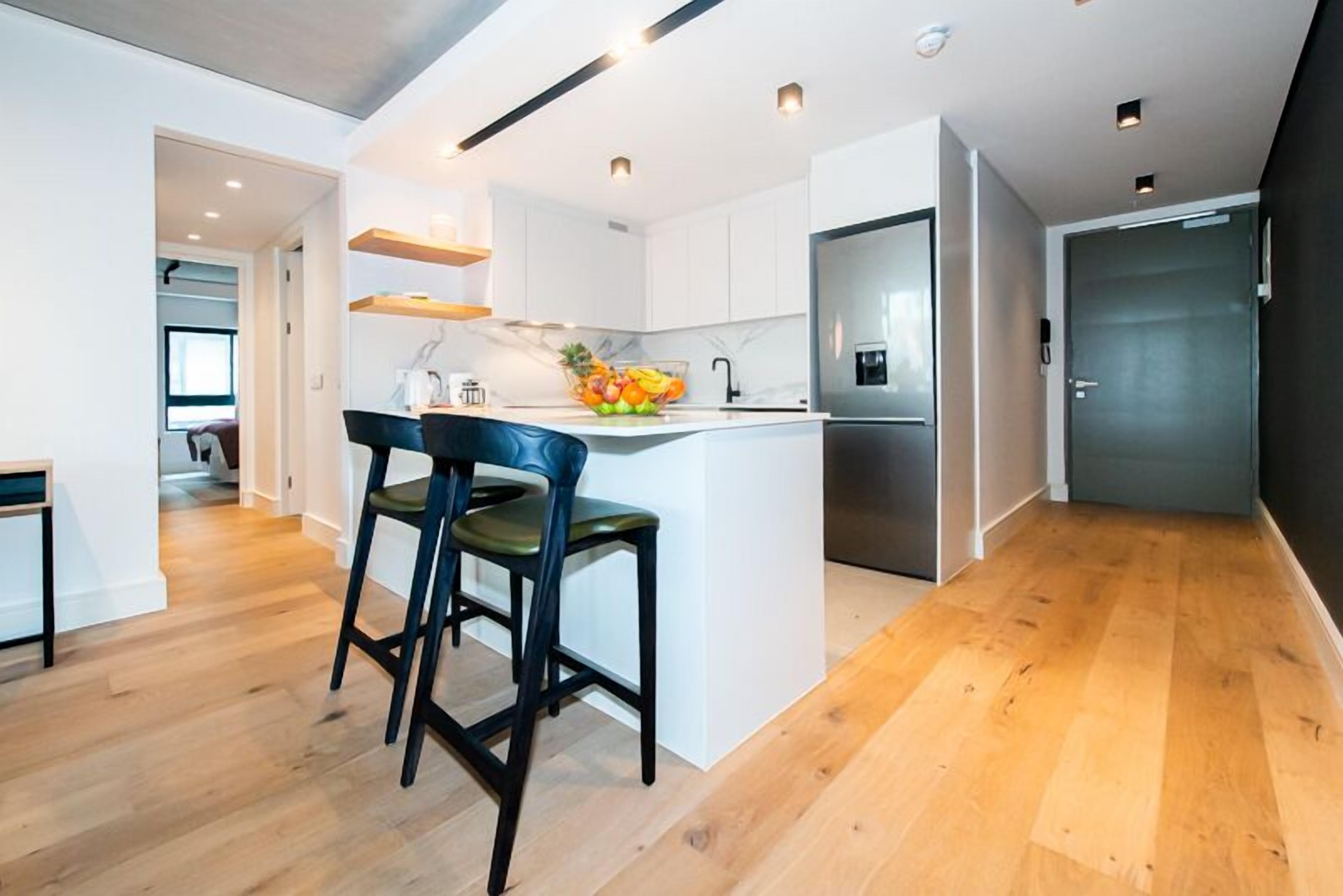 A modern kitchen with white cabinets, a stainless steel refrigerator, and a fruit bowl on the island.