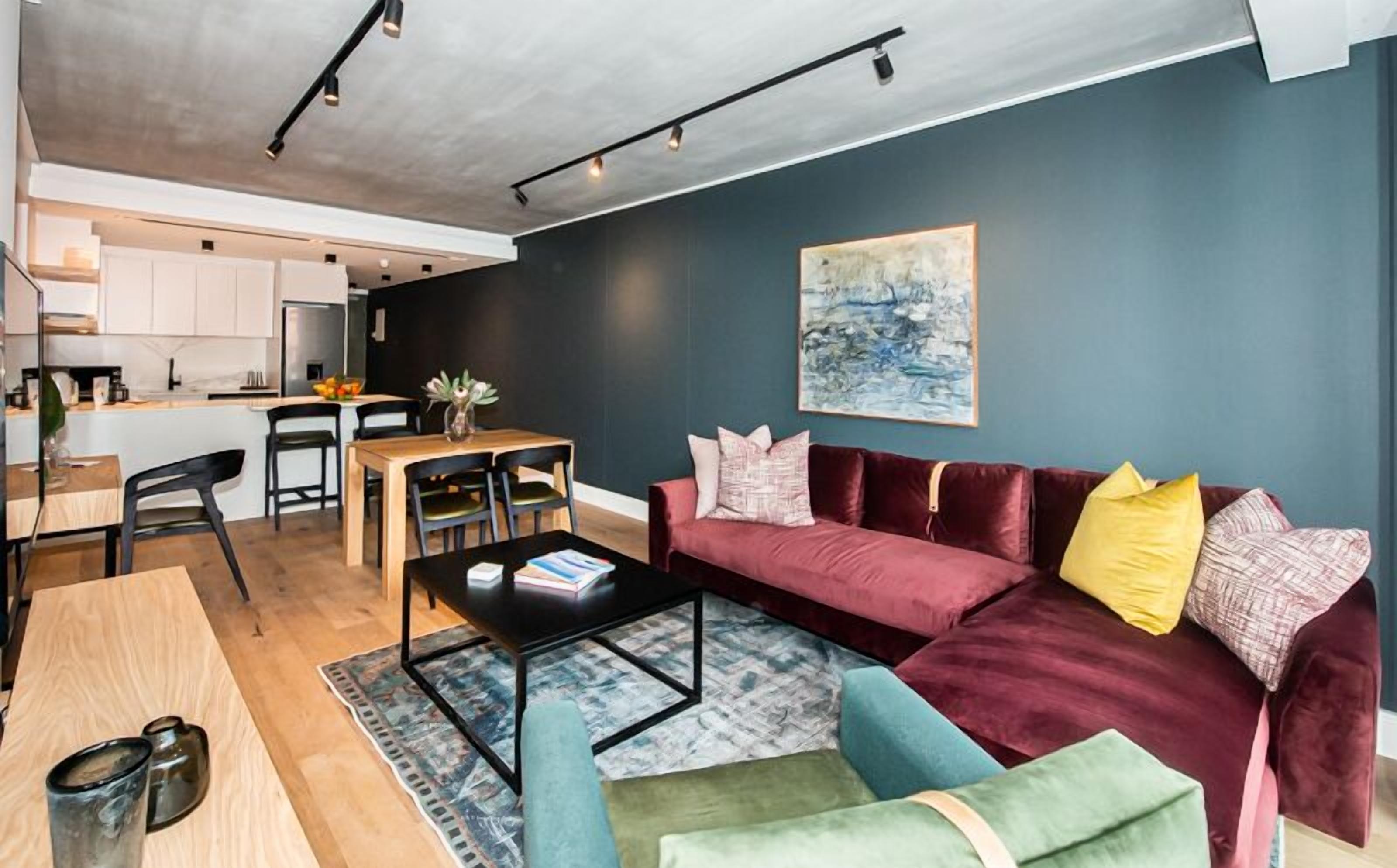 A modern living room with a red sofa, a coffee table, and a dining area with a kitchen in the background.