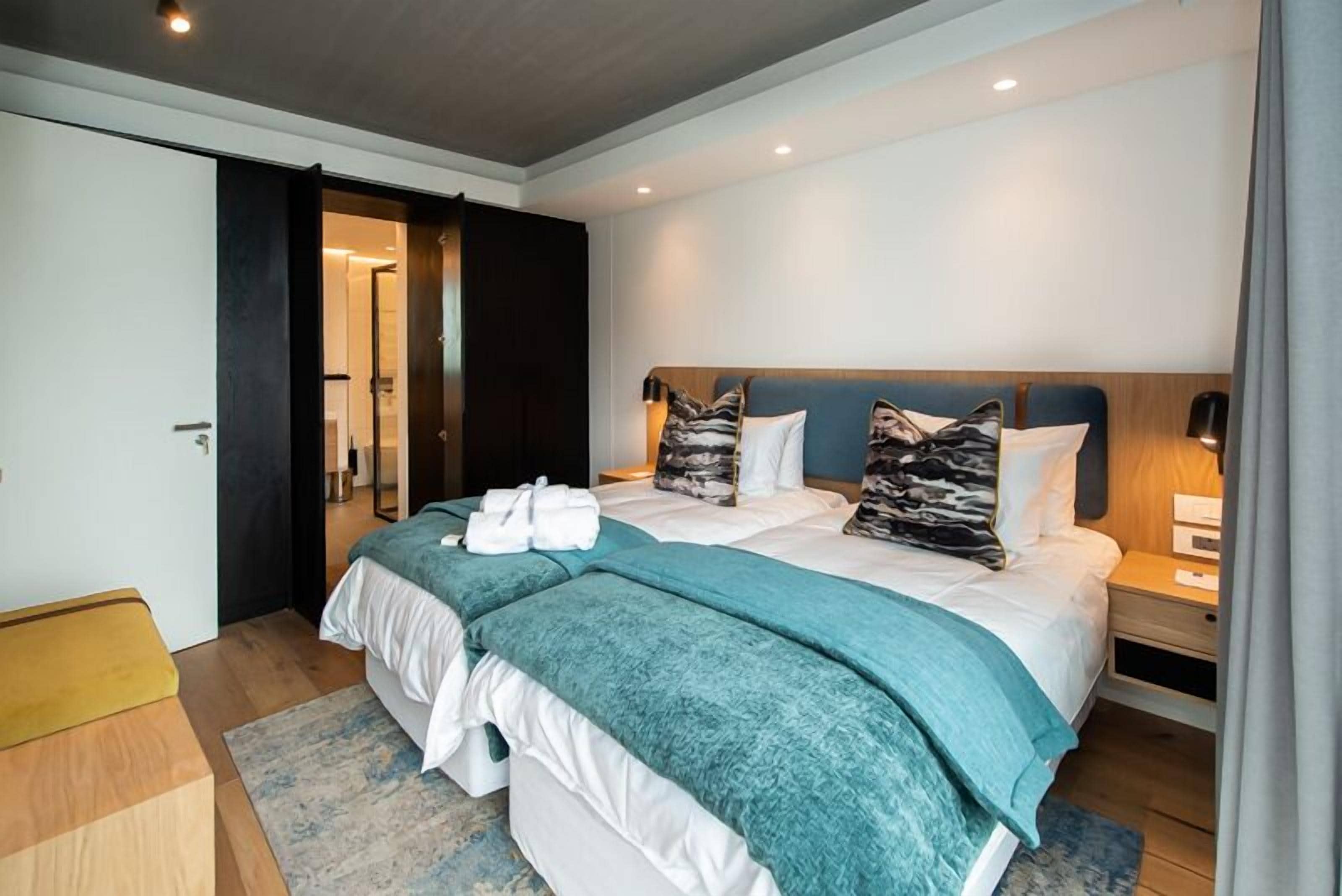A modern hotel room with a large bed, two bedside tables, and a wardrobe.
