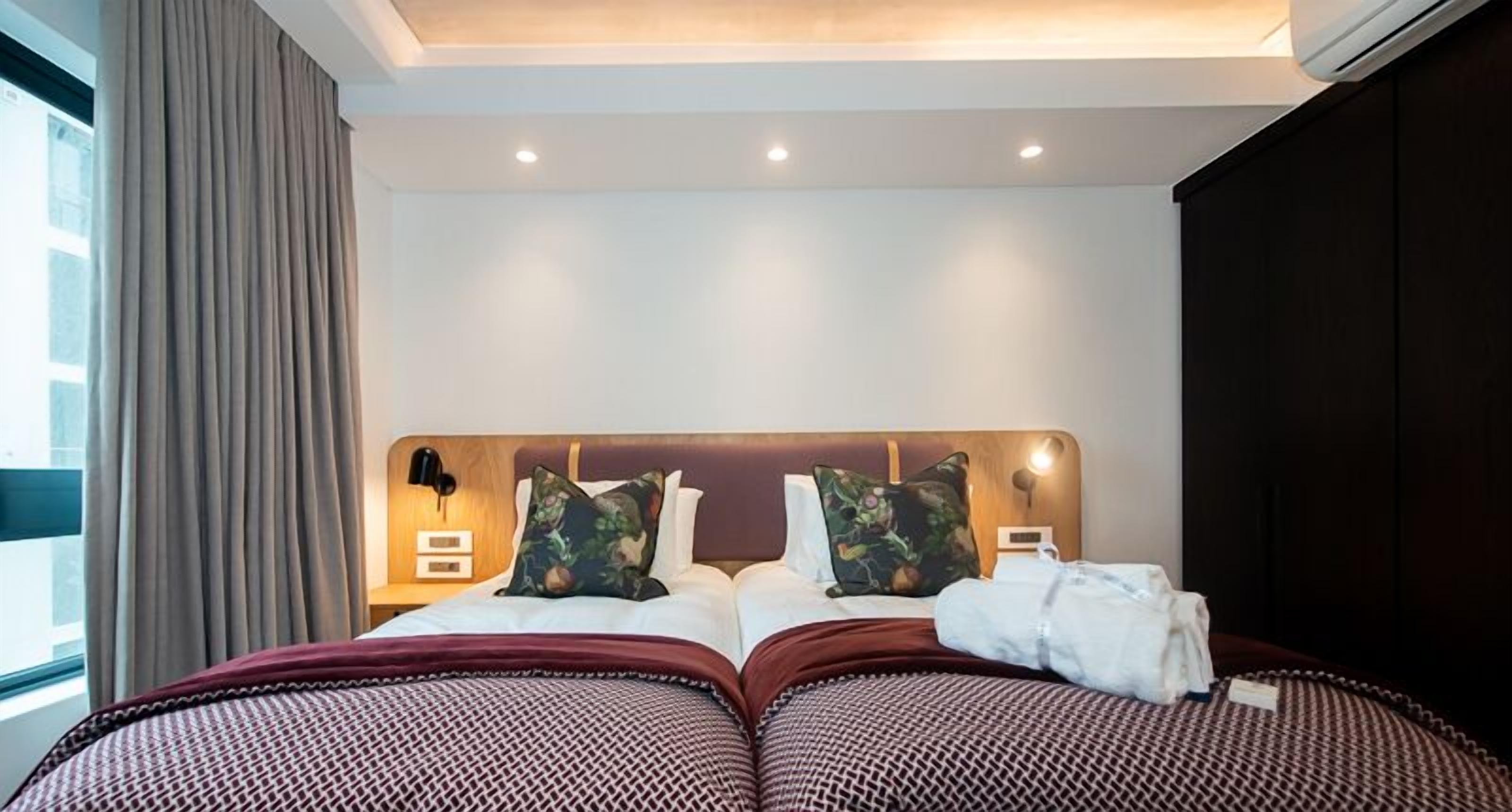 A hotel room with a large bed, two pillows, a nightstand, and a window with curtains.