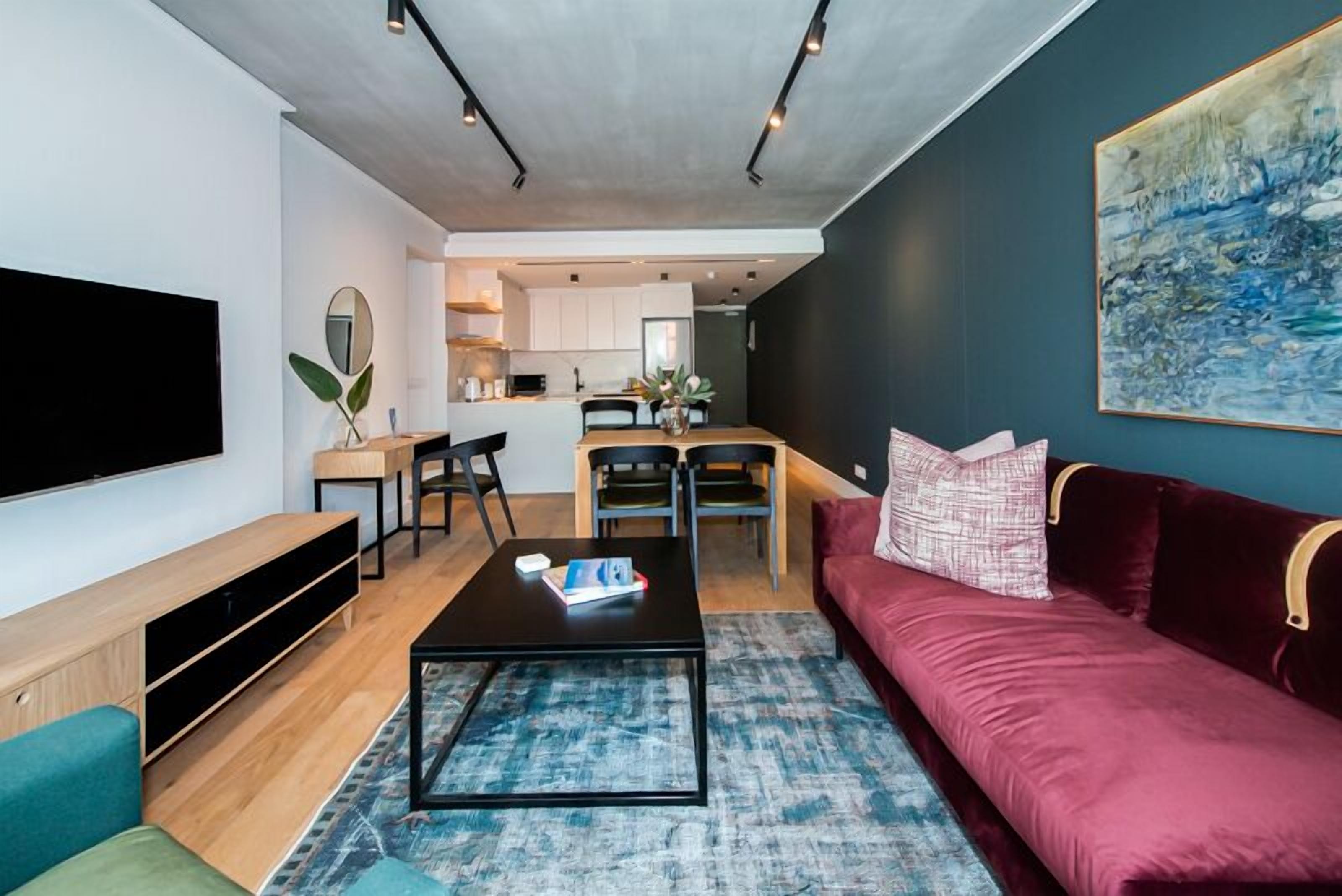 A modern living room with a flat-screen TV, a red sofa, a coffee table, and a dining area with chairs.
