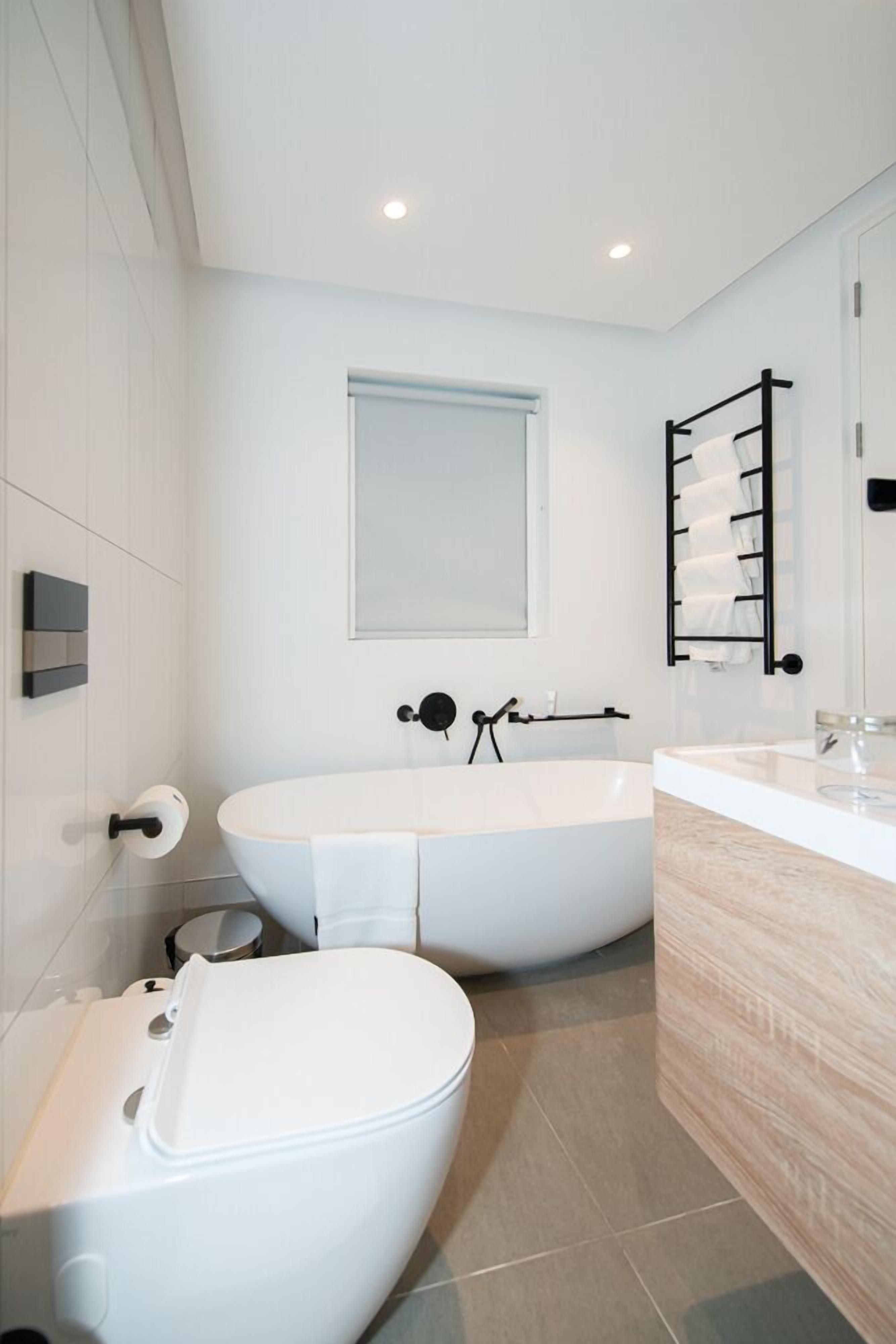 A modern bathroom with a freestanding bathtub, a toilet, and a vanity with a mirror.