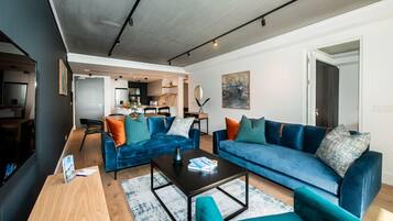 A modern living room with two blue sofas, a coffee table, and a dining area in the background.