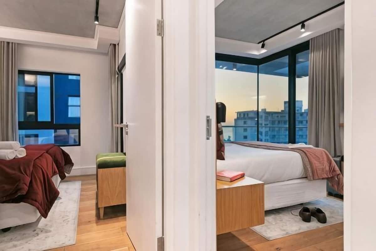 A modern bedroom with a bed, bedside table, and a view of the city.