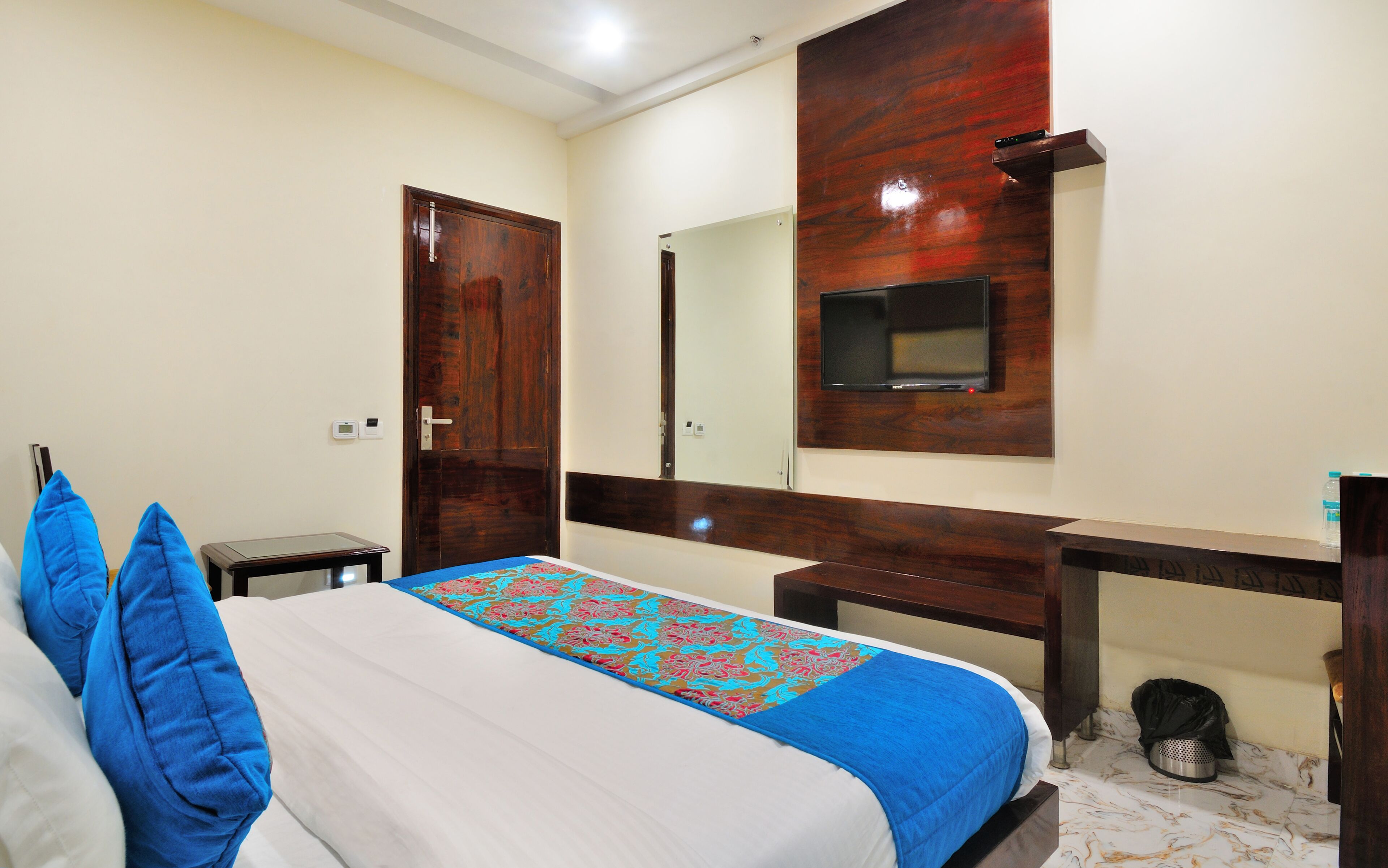 Una habitación de hotel con cama, escritorio, espejo y televisión.