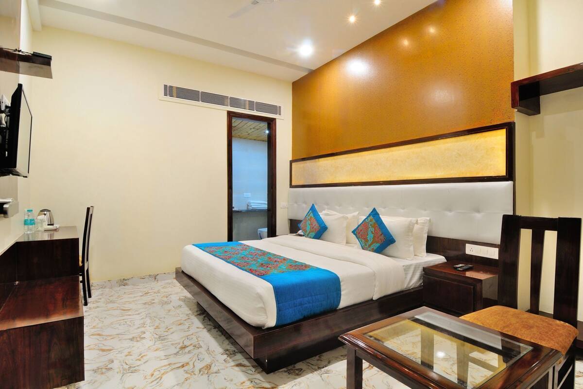 A hotel room with a bed, bedside table, chair, and a desk with a mirror.