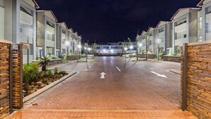 A hotel entrance with a paved driveway leading to a building, flanked by two-story structures with balconies and a central entrance.
