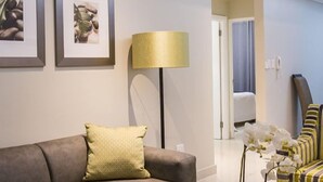 A modern living room with a grey sectional sofa, a small table, and a floor lamp. There are framed pictures on the wall and a potted plant on the table.