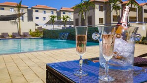 A poolside setting with a table holding two glasses of champagne and a bottle in a bucket.
