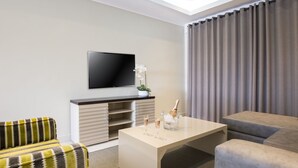 A modern living room with a flat-screen TV, a coffee table with drinks, a sofa, and a cabinet.