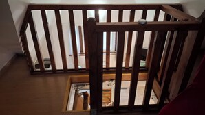 Una ringhiera di legno con corrimano in metallo, un pavimento in legno e vista su un ambiente interno.