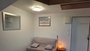Una stanza con un divano grigio, un tavolino, un quadro appeso al muro e una porta.