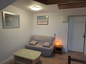 A room with a grey sofa, a small table, a framed picture on the wall, and a door.