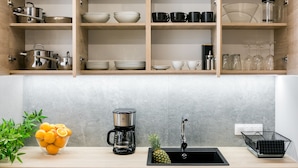 Une cuisine avec des étagères en bois, une machine à café, un évier et un saladier rempli de fruits.