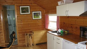 A wooden cabin interior with a shower, a dining area, and a kitchen with a sink and coffee maker. - Sæbø Camping (Eidfjord)