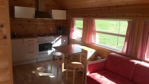 A cozy cabin interior with a kitchenette, a dining area, and a red sofa. - Sæbø Camping (Eidfjord)