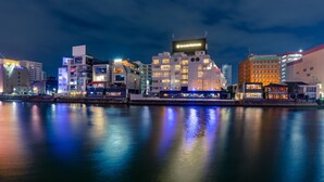 A waterfront cityscape at night with illuminated buildings reflecting on the water. - The OneFive Villa Fukuoka (Fukuoka)