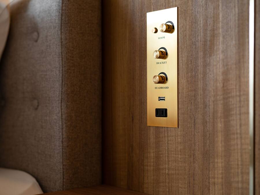 A wall-mounted control panel with four knobs labeled "ROOM," "BRACKET," "HEADBOARD," and a power button.