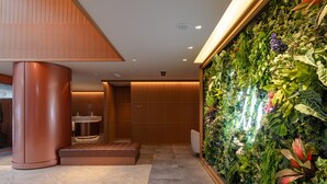 A modern lobby with a large vertical garden, a curved metallic column, and a reception area with a sink. - The OneFive Villa Fukuoka (Fukuoka)