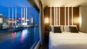A hotel room with a large bed, a nightstand, and a view of a cityscape and river at dusk. - The OneFive Villa Fukuoka (Fukuoka)