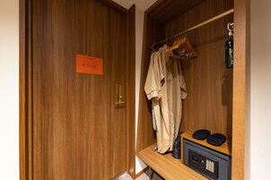 A wooden wardrobe with a hanging rack, a safe, and a pair of slippers on the shelf.