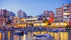 Una zona ribereña con barcos amarrados, un edificio con el letrero 'DOLCE VITA' y una hilera de edificios de varios pisos.