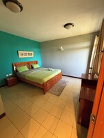 Un dormitorio con cama, mesita de noche, cómoda, estante en la pared y un marco de fotos.