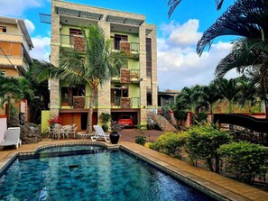 A multi-story building with a swimming pool, outdoor seating, and palm trees. - Résidence Padma (Flic-en-Flac)