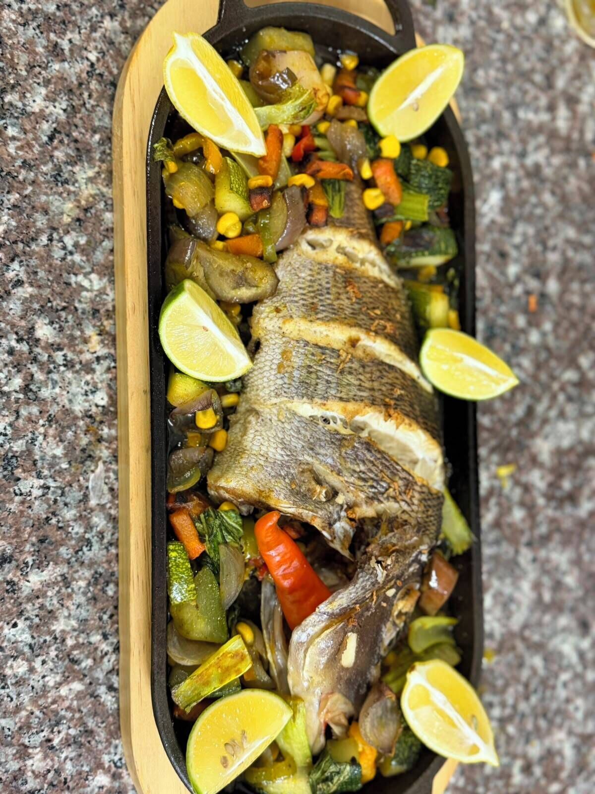 Un poisson entier, accompagné de légumes, dans une poêle.