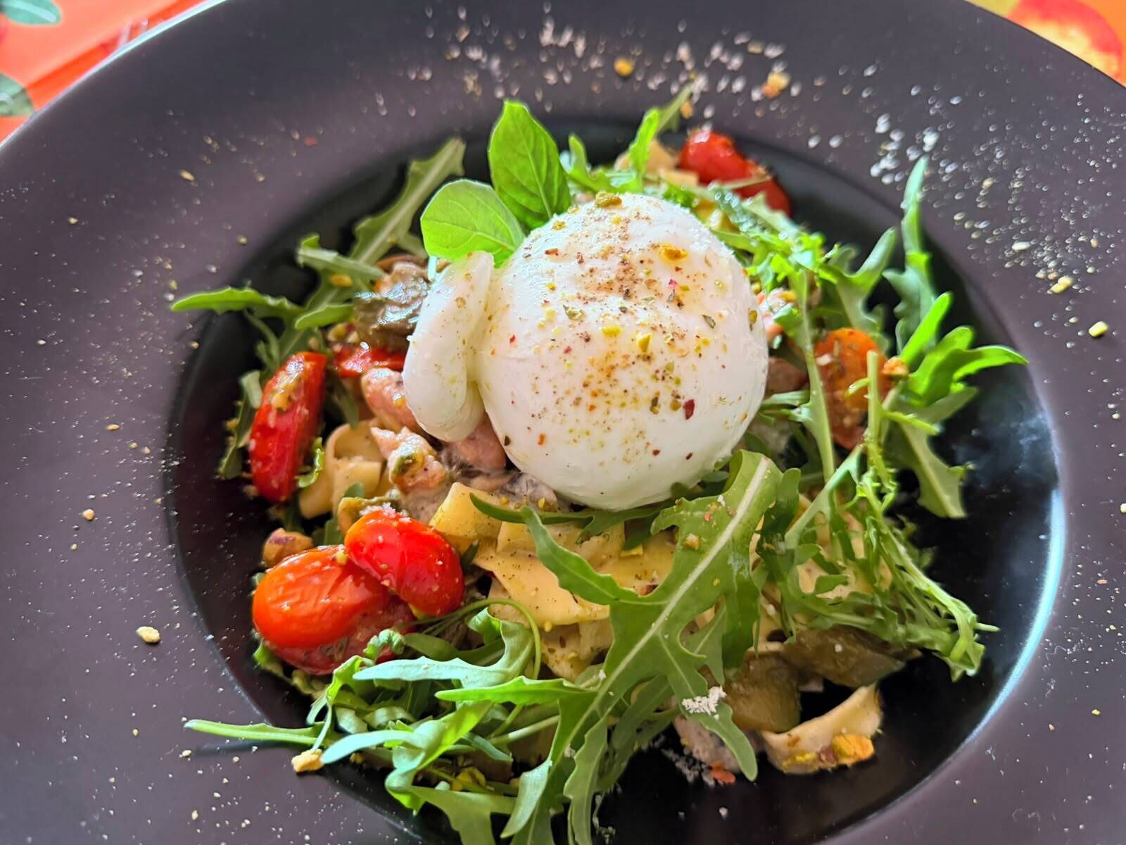 A dish with a poached egg on top, surrounded by greens and tomatoes.