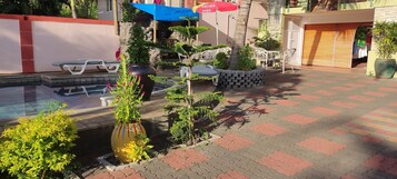 Un área junto a la piscina con un conjunto de asientos, una jardinera con plantas y un sendero empinado.