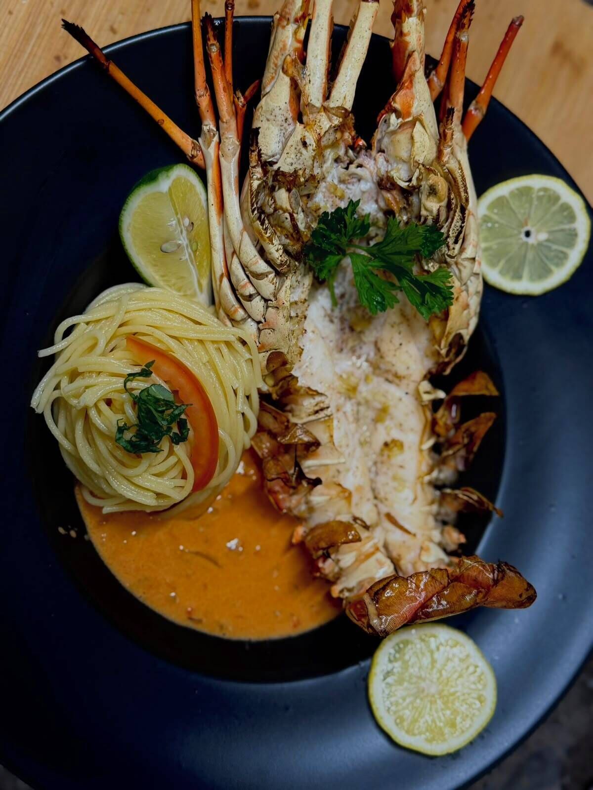 A seafood dish with a lobster tail, spaghetti, and a sauce on a dark plate.