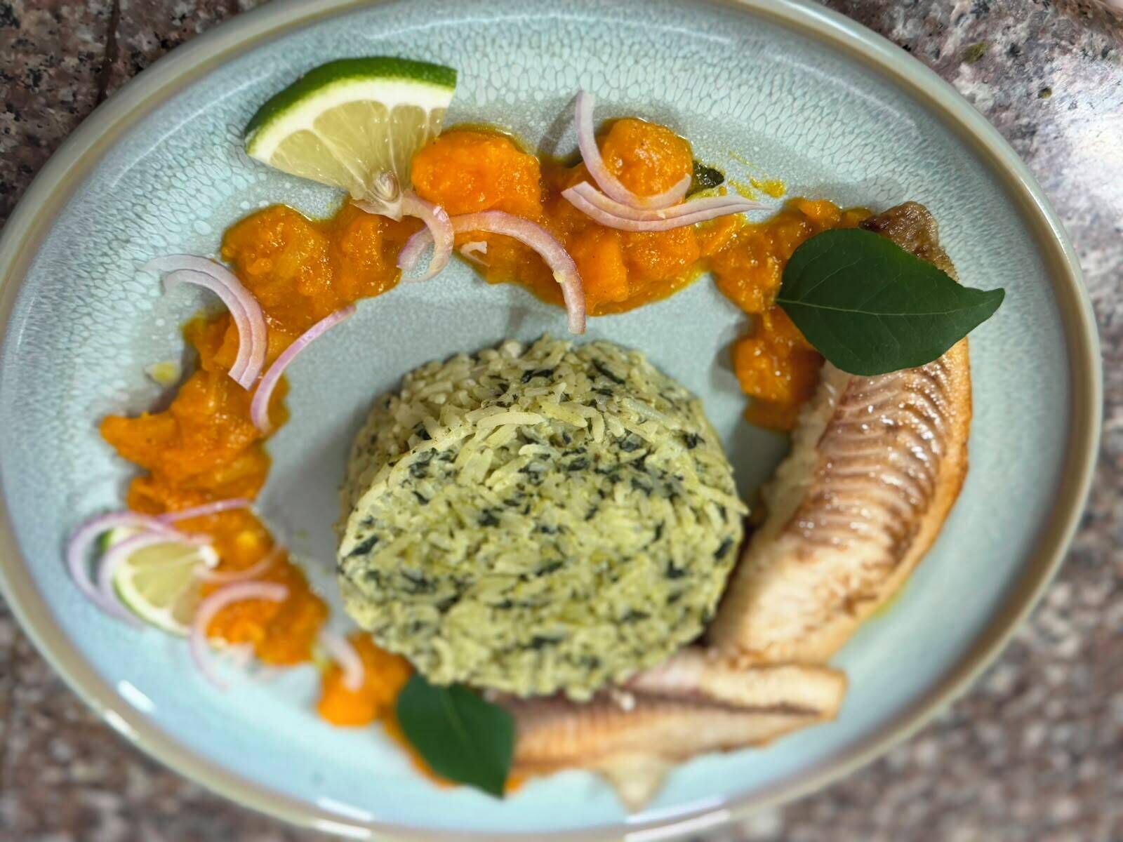 Un plato con pescado, un acompañamiento de hierbas verdes y una rodaja de lima.