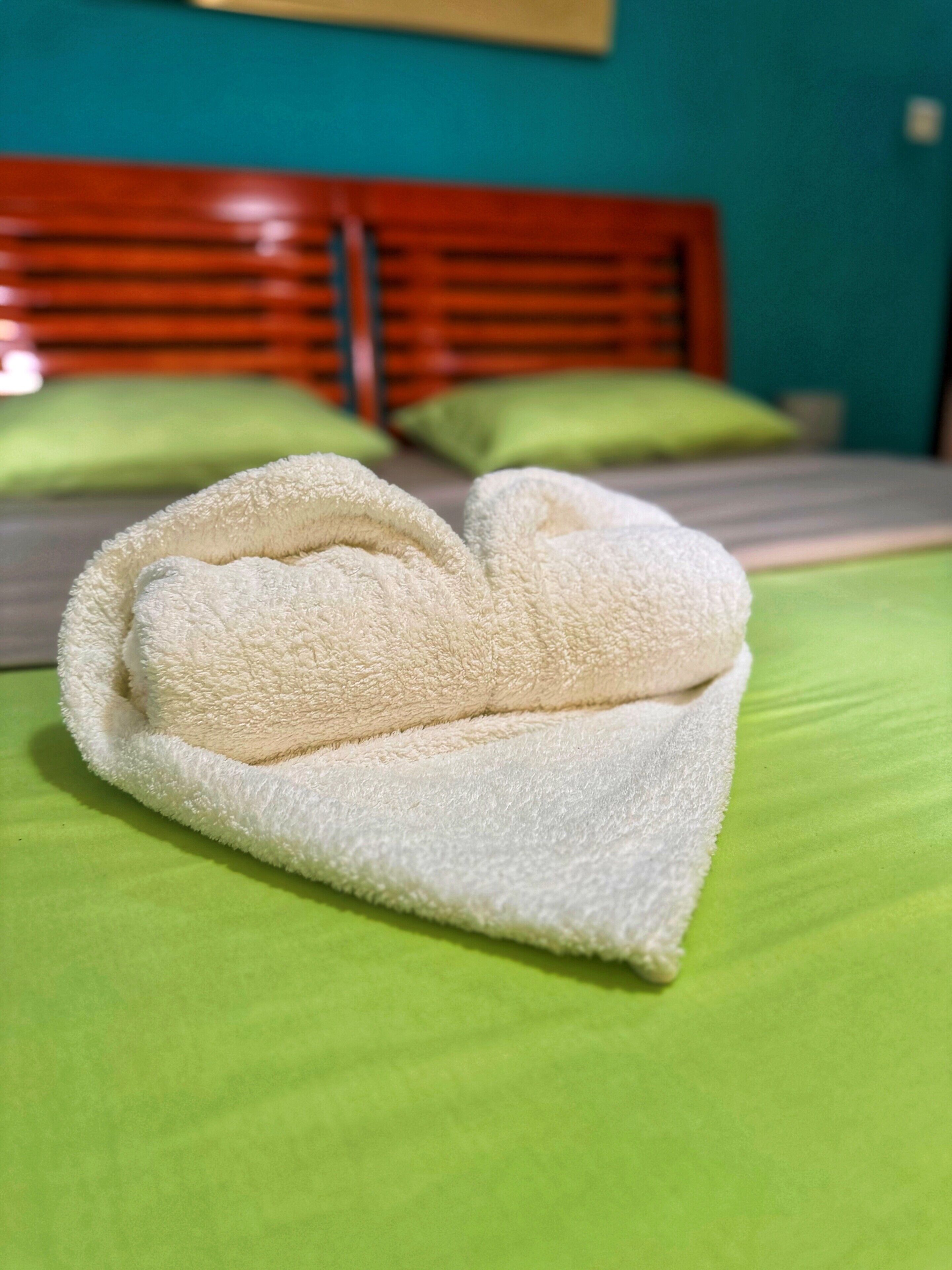 A neatly folded towel on a green bedspread in a hotel room with a wooden headboard and green pillows.