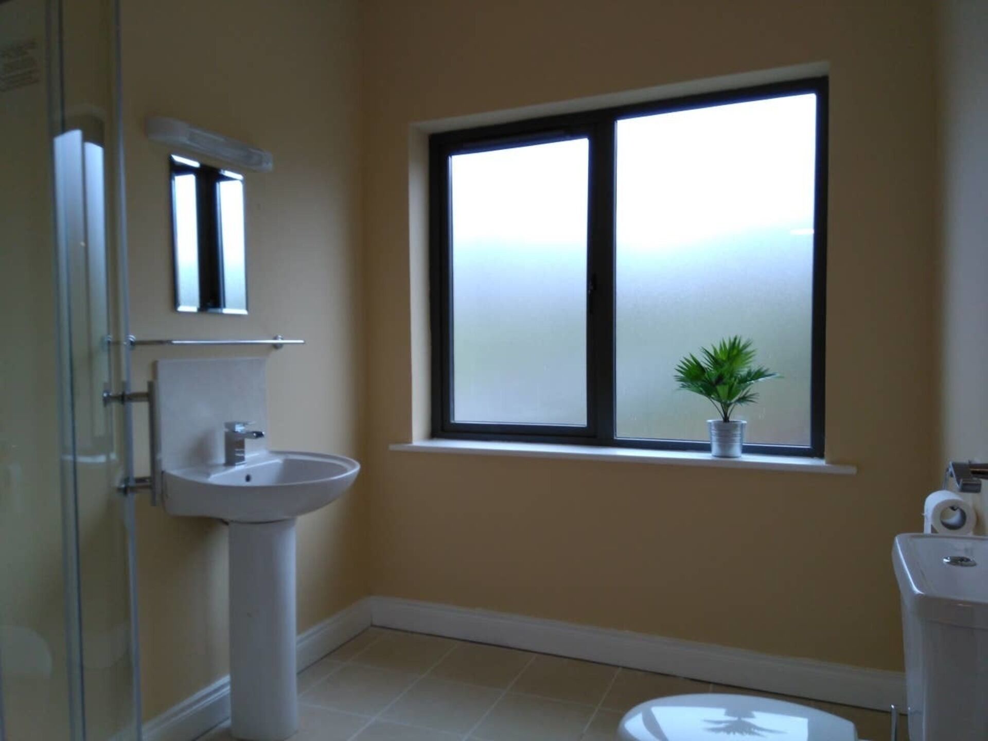 Une salle de bain avec un lavabo, des toilettes et une fenêtre agrémentée d’une plante.